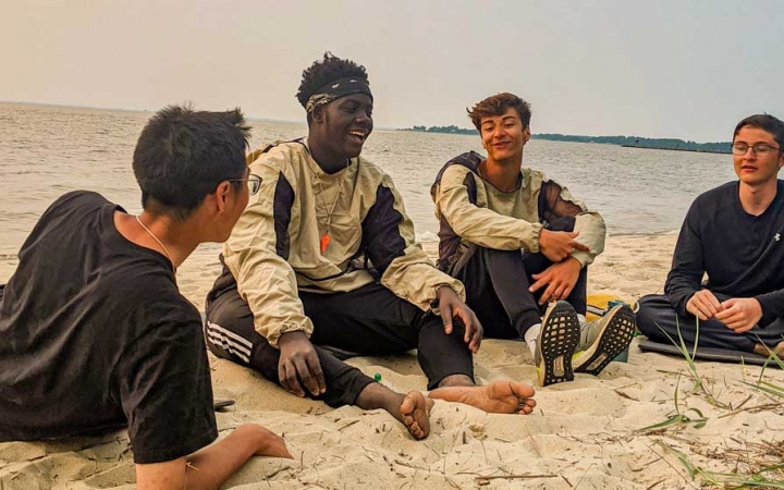 a group of teens sit on a beach while on a kayaking course